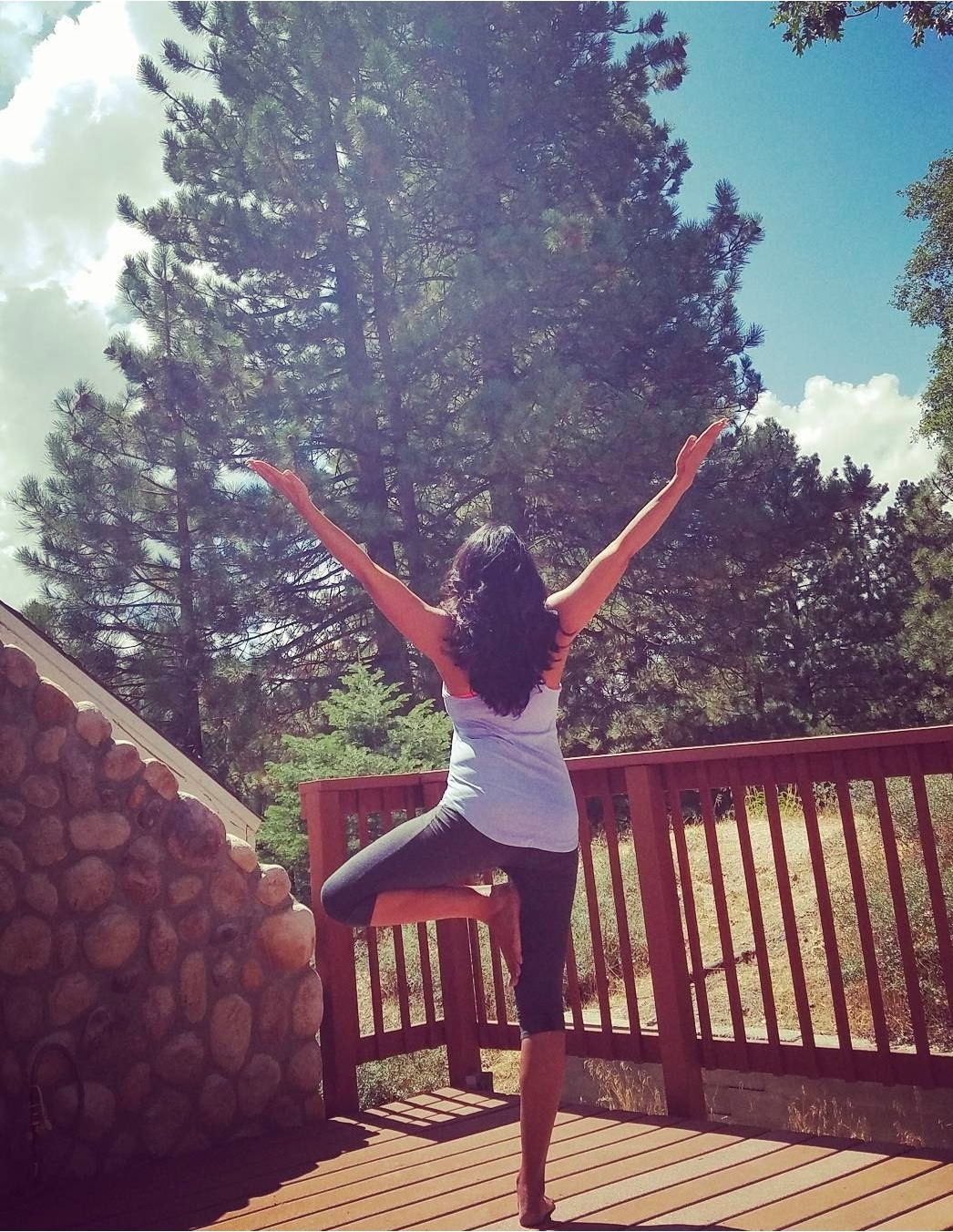 Jeena in tree pose on a mountain deck surrounded by nature