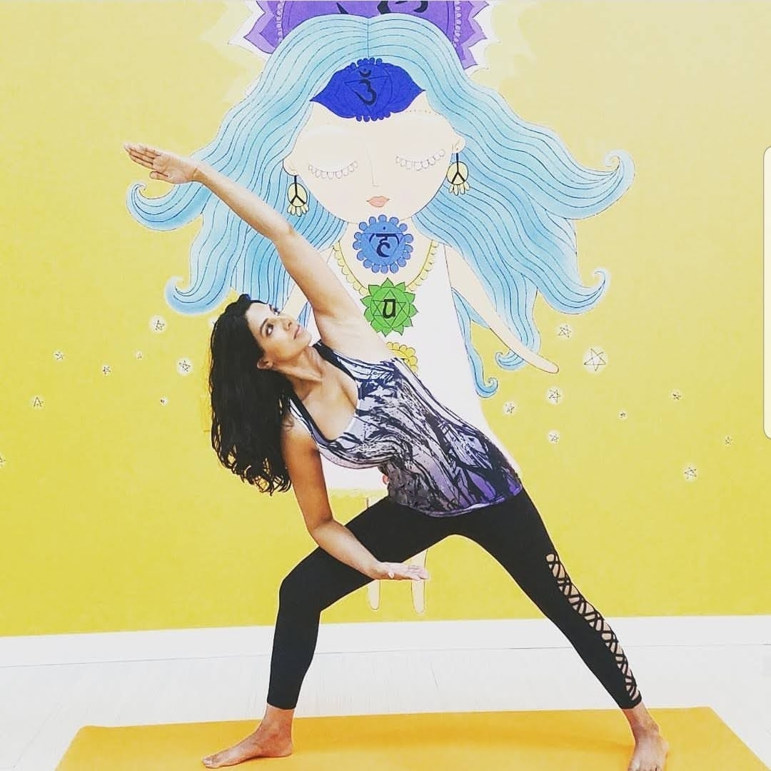 Jeena in warrior pose with chakra mural at JeeNamaste studio